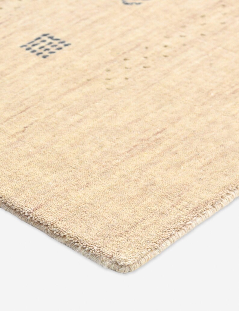 Puede incluir: Alfombra beige con superficie texturizada y dise&ntilde;o geom&eacute;trico. La alfombra presenta un patr&oacute;n cuadrado y puntos dispersos en un tono beige m&aacute;s oscuro. El borde de la alfombra est&aacute; cuidadosamente terminado con un borde sutil.