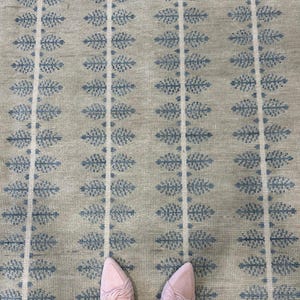 May include: A beige rug with a repeating pattern of blue leaf-like shapes and vertical white stripes. The rug has a textured appearance. Pink shoes are visible at the bottom of the image.