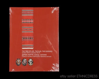 May include: A red book with the title "THE TREE OF LIFE, THE SUN, THE GODDESS" in English and Ukrainian. The cover features a vertical design with red, black, and white patterns, and three decorated eggs.