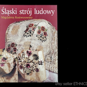 May include: Book cover featuring a close-up of a traditional Polish folk costume, with intricate embroidery and embellishments. The title of the book is "Śląski strój ludowy" by Magdalena Rostworowska.