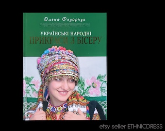 May include: A book cover with a green background and the title "Українські народні прикраси з бісеру" in gold lettering. The cover features a woman wearing a traditional Ukrainian headdress adorned with colorful beads.