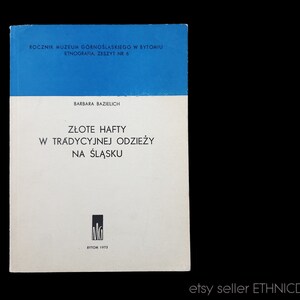 May include: A blue book cover with the title "Zlote Hafty w Tradycyjnej Odziezy na Slasku" by Barbara Bazielich. The book is a publication of the Museum of Upper Silesia in Bytom, Poland.