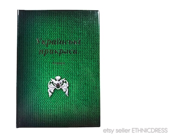 Può includere: Un libro verde con il titolo "Українські прикраси" in lettere dorate. La copertina del libro presenta un design decorativo argento e nero.