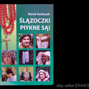 May include: A green book cover with the title "Ślązoczki Piękne Są!" in Polish. The book cover features a red rosary, a gold cross, and several photos of people wearing traditional Polish clothing.