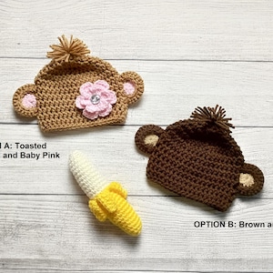 May include: Two crocheted baby hats, one in toasted almond with baby pink accents and a pink flower, the other in brown and tan. A crocheted banana is also present. Text reads "OPTION A: Toasted Almond and Baby Pink" and "OPTION B: Brown and Tan."