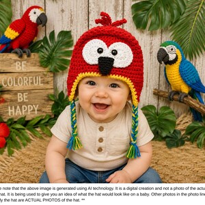 Puede incluir: Un beb&eacute; sonriente con un gorro de loro rojo de ganchillo con ojos blancos, pico negro y ribete amarillo. El gorro tiene trenzas laterales. Dos loros de ganchillo y el texto "BE COLORFUL BE HAPPY" est&aacute;n en el fondo.