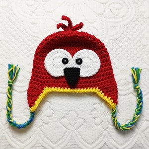 Puede incluir: Un gorro rojo hecho a mano con dise&ntilde;o de p&aacute;jaro. El gorro presenta c&iacute;rculos oculares blancos, pupilas negras y un pico negro. Tiene ribetes amarillos y orejeras trenzadas en azul, verde y amarillo.