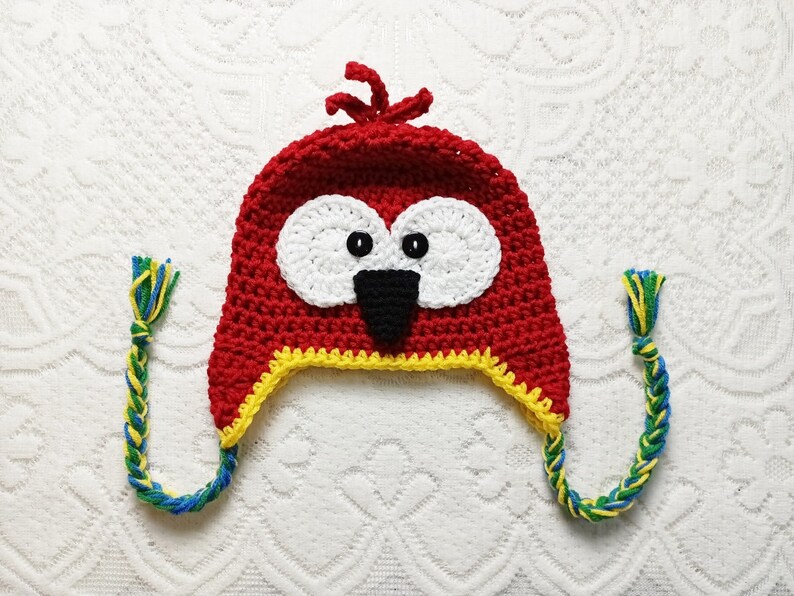 Puede incluir: Un gorro rojo hecho a mano con dise&ntilde;o de p&aacute;jaro. El gorro presenta c&iacute;rculos oculares blancos, pupilas negras y un pico negro. Tiene ribetes amarillos y orejeras trenzadas en azul, verde y amarillo.