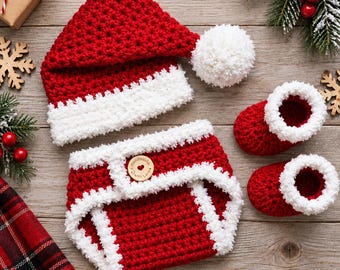 May include: A red and white crocheted set consisting of a pointed hat with a white pom-pom, a diaper cover with a wooden button featuring the text Handmade with Love, and two booties. Each piece features a textured red base and white trim.