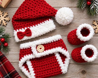 May include: A red and white crocheted set consisting of a pointed hat with a white pom-pom and a small red bow, a diaper cover with a wooden button labeled Handmade with Love, and a pair of matching booties with white fuzzy trim cuffs.