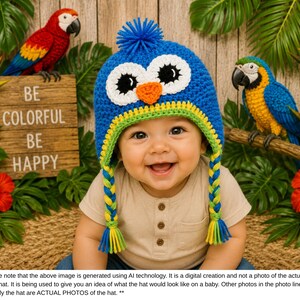 Puede incluir: Un beb&eacute; sonriente con un gorro de b&uacute;ho azul tejido con ojos blancos, pico naranja y ribetes amarillos y verdes. El gorro tiene trenzas laterales. El fondo incluye loros, flores y el texto "BE COLORFUL BE HAPPY."