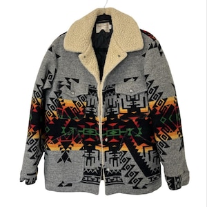 May include: A gray wool jacket with a cream-colored shearling collar and a colorful geometric pattern in black, red, orange, and yellow. The jacket has two chest pockets and two lower pockets.