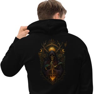 May include: A black hooded sweatshirt featuring a detailed graphic on the back. The design depicts a hooded skeletal figure with antlers, surrounded by roses, crescent moons, and a glowing sun, with a fiery, sword-like element at the base.