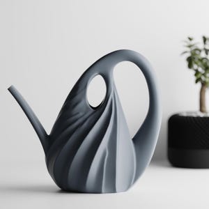 May include: A matte slate gray watering can featuring a sculptural, spiraling pleated design. The vessel has a curved handle that forms an integrated loop at the top and a slender, angled spout extending from the side for controlled water flow.