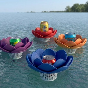 Pode incluir: Quatro porta-bebidas flutuantes coloridos em forma de flores de lótus, cada um segurando uma lata de refrigerante ou chá gelado. Os porta-bebidas são em tons de vermelho, laranja, roxo e azul, com uma base de cesta branca. Flutuam na água.