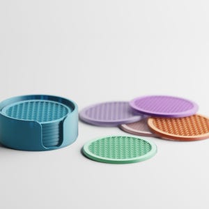 Pode incluir: Um conjunto de bases para copos circulares com um padrão geométrico texturizado na superfície. As bases vêm em várias cores, incluindo azul, verde, roxo e laranja, e são guardadas num suporte cilíndrico azul a condizer com uma abertura.