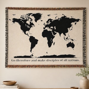 Peut inclure: Une tapisserie tissée avec un motif de carte du monde noir sur fond crème. La tapisserie a une bordure à franges et le texte "Go therefore and make disciples of all nations" est inclus.