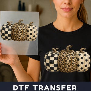 May include: A DTF transfer sheet and a black t-shirt featuring a graphic of three pumpkins. The left pumpkin has a black and white checkered pattern, the centre pumpkin has a brown leopard print, and the right pumpkin has black polka dots.