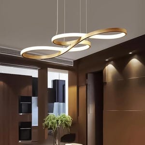 Può includere: Moderna lampada a sospensione a LED color oro con un esclusivo design a forma di infinito. La lampada è appesa al soffitto, illuminando una sala da pranzo con un tavolo e sedie scure. La luce emana un bagliore caldo.