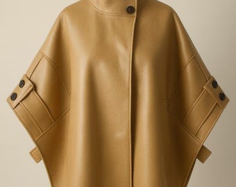May include: A tan-colored cape-style jacket with a high collar and two dark buttons. The jacket features short sleeves with buttoned cuffs and decorative flaps. The garment is displayed on a mannequin.