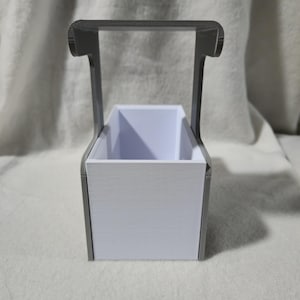 May include: A white rectangular container with a grey handle. The container has a textured surface and a rectangular opening. The handle is arched and connects to the sides of the container.