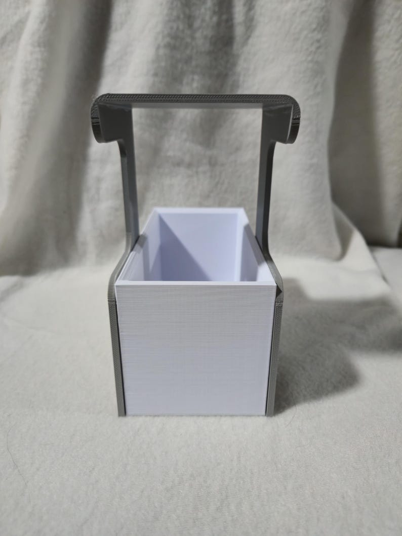 May include: A white rectangular container with a grey handle. The container has a textured surface and a rectangular opening. The handle is arched and connects to the sides of the container.