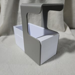 May include: A grey and white organiser with a handle. The organiser has a rectangular white box with a grey handle attached to the side. The handle curves over the top of the box. The organiser is on a white surface.