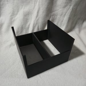 May include: A black, rectangular organiser with two compartments. The organiser is made of a matte material and has a simple, modern design. The compartments are divided by a vertical divider.