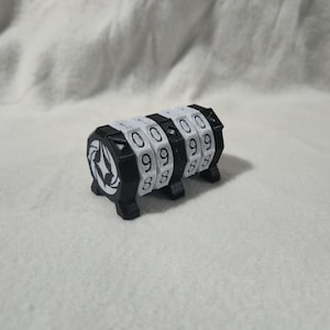 Può includere: Un lucchetto a combinazione in bianco e nero con quattro quadranti numerici rotanti. Ogni quadrante mostra numeri bianchi su sfondo nero. Il lucchetto ha un emblema decorativo su ciascuna estremità.