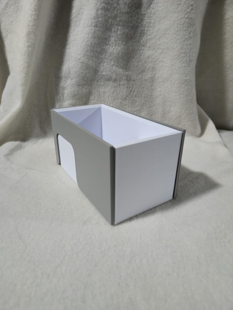 May include: A rectangular storage box with a white interior and grey exterior trim. The box has a cutout on one side and is sitting on a white, textured surface. The box is empty.
