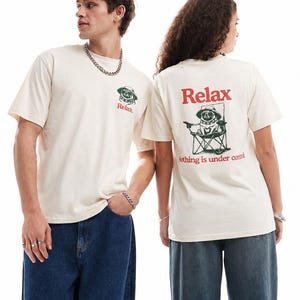 Könnte beinhalten: Cremefarbenes Kurzarm-T-Shirt mit einer kleinen Grafik eines Mopses mit Hut auf der Brust und dem Text Relax. Die Rückseite zeigt eine große Grafik eines Mopses mit Hut in einem Klappstuhl mit dem Text Relax und Nothing is under control.