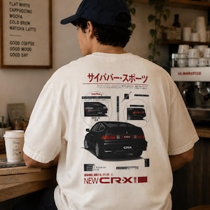 May include: An off-white short-sleeve t-shirt featuring a graphic print on the back. The design includes a black car illustration, technical diagrams, and Japanese text. The text includes "NEW CR-X" in red and "サイババー・スポーツ" at the top.