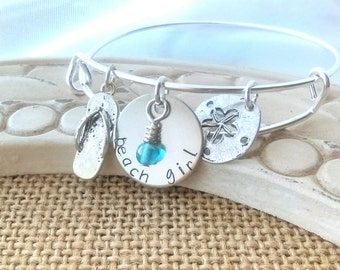 May include: Silver charm bracelet with a flip-flop charm, a round charm with the words "beach girl" and a turquoise bead, and a charm with a starfish design.