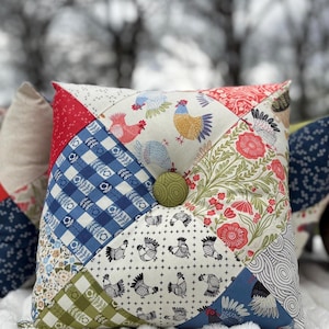 May include: A collection of decorative throw pillows with patchwork designs. The pillows feature various patterns, including floral, gingham, and rooster motifs. Each pillow has a button in the center. The color palette includes red, blue, green, and white.