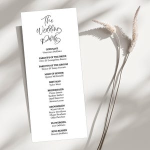 May include: A white wedding program featuring the words "The Wedding Party" in elegant calligraphy. The program lists the officiant, parents of the bride and groom, maid of honour, best man, bridesmaids, groomsmen, flower girl, and ring bearer.