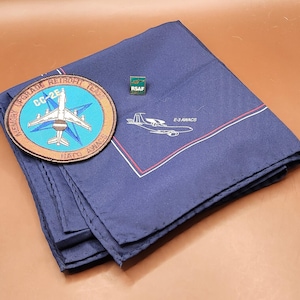May include: A navy blue handkerchief with a white and red border, a patch with an airplane design, and a green pin with the text "RSAF". The patch reads "MEMORY UPGRADE RETROFIT TEAM CC-2E NATO AWACS".