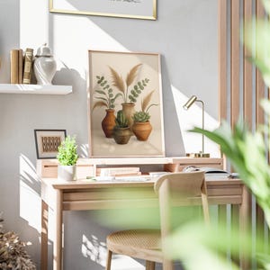 May include: A framed art print featuring a watercolor illustration of plants in terracotta pots. The artwork is displayed on a wooden desk with a small lamp, books, and a chair. The scene is bathed in natural light, creating a warm, inviting atmosphere.
