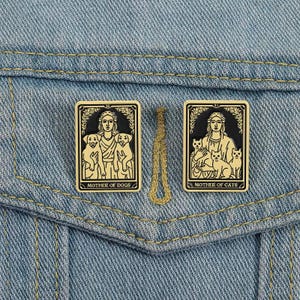 May include: Two rectangular enamel pins with gold borders and black and gold illustrations. One pin reads "MOTHER OF DOGS" and depicts a woman with two dogs. The other pin reads "MOTHER OF CATS" and depicts a woman with three cats.