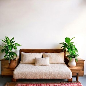 Puede incluir: Una cama de madera con un colchón y almohadas texturizadas de color crema. Dos mesitas de noche de madera flanquean la cama, cada una con una planta en maceta. Una alfombra roja estampada se encuentra al pie de la cama, creando un ambiente acogedor en el dormitorio.