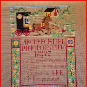 May include: A cross-stitch sampler with a colorful scene of a horse-drawn carriage, a house, and flowers. The alphabet, numbers, and the text "stitched by LFF in the year 1989" are included.