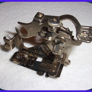 May include: A silver sewing machine foot with a black plastic piece and a metal dial marked "Singer 1244".