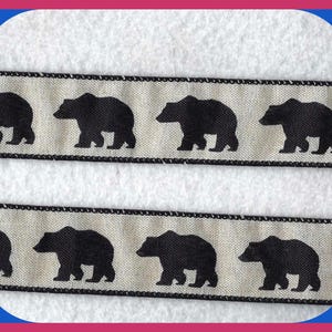 May include: Two strips of beige ribbon with a repeating pattern of black bear silhouettes. The ribbon edges are trimmed with a black border. The bears are evenly spaced across the ribbon, creating a rustic and outdoorsy design.