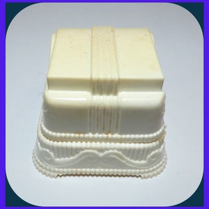 May include: A white plastic ring box with a decorative design around the base. The top of the box has a raised, ribbed design.