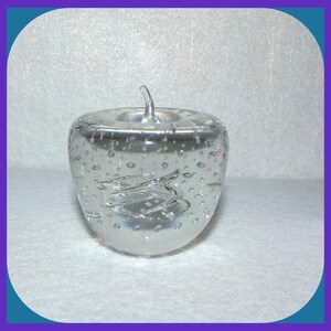 May include: A clear glass apple paperweight with a swirl design and air bubbles throughout.