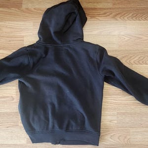May include: A dark navy blue hooded sweatshirt with a full zipper closure. The sweatshirt has a hood and long sleeves. The garment is made of a soft, comfortable material. The sweatshirt is shown lying flat on a wooden surface.