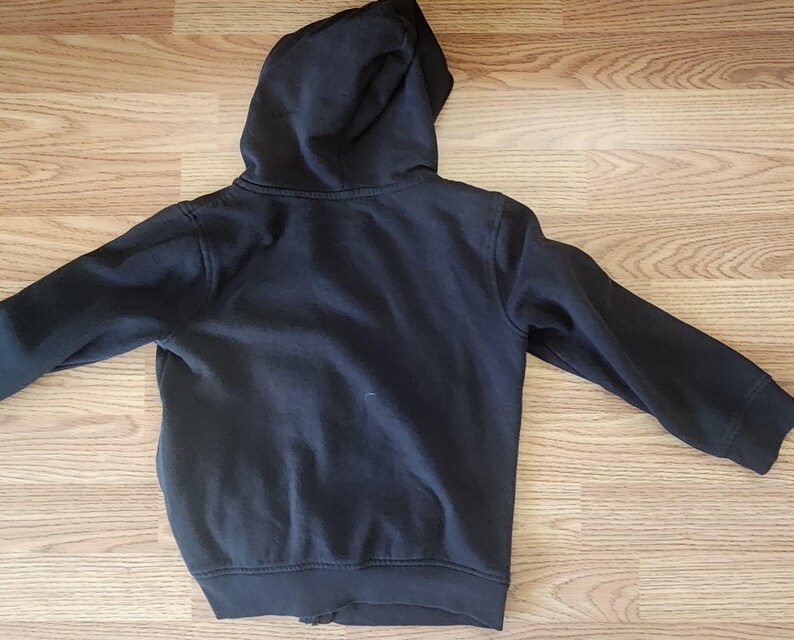 May include: A dark navy blue hooded sweatshirt with a full zipper closure. The sweatshirt has a hood and long sleeves. The garment is made of a soft, comfortable material. The sweatshirt is shown lying flat on a wooden surface.
