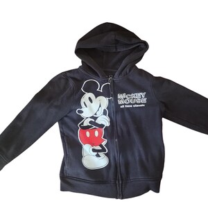 May include: Black zip-up hoodie featuring a large graphic of Mickey Mouse in white, red, and black. The hoodie has a hood and the text "Mickey Mouse all time classic" on the right side. The hoodie is made of a soft material.