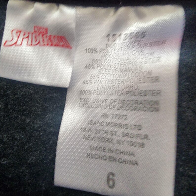 Puede incluir: Una etiqueta de ropa blanca con el logotipo de Marvel Spider-Man en rojo. La etiqueta incluye informaci&oacute;n sobre la composici&oacute;n de la tela, incluyendo poli&eacute;ster y algod&oacute;n, y la talla, que es un 6. La etiqueta tambi&eacute;n incluye la informaci&oacute;n del fabricante.