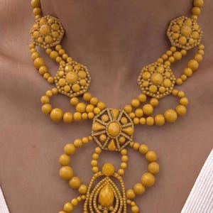 May include: A bright yellow statement necklace featuring a series of round beads and intricate geometric components. The design includes hexagonal and teardrop-shaped elements with faceted centres, all connected by multiple strands of smooth yellow beads.