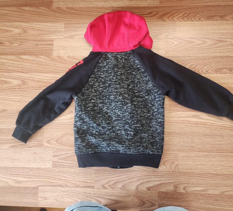 Puede incluir: Una sudadera con capucha negra y gris con capucha roja. La sudadera tiene mangas negras y un cuerpo gris y negro moteado. La palabra "RED" est&aacute; impresa en la manga izquierda. La sudadera est&aacute; hecha de un material suave y c&oacute;modo.